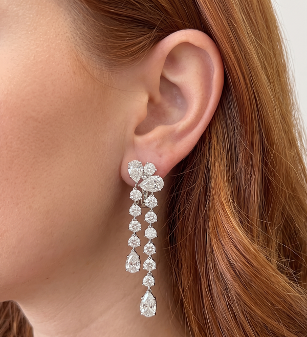 A close-up of a woman's ear wearing a long drop earring made of clear teardrop-shaped gemstones in a silver-toned setting. The product is shown on skin, so the subject_type is classified as Lifestyle.