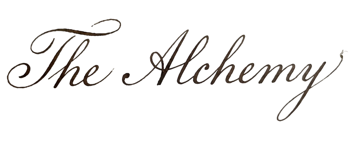 Elegant cursive calligraphy text reading The Alchemy in dark ink on a white background.