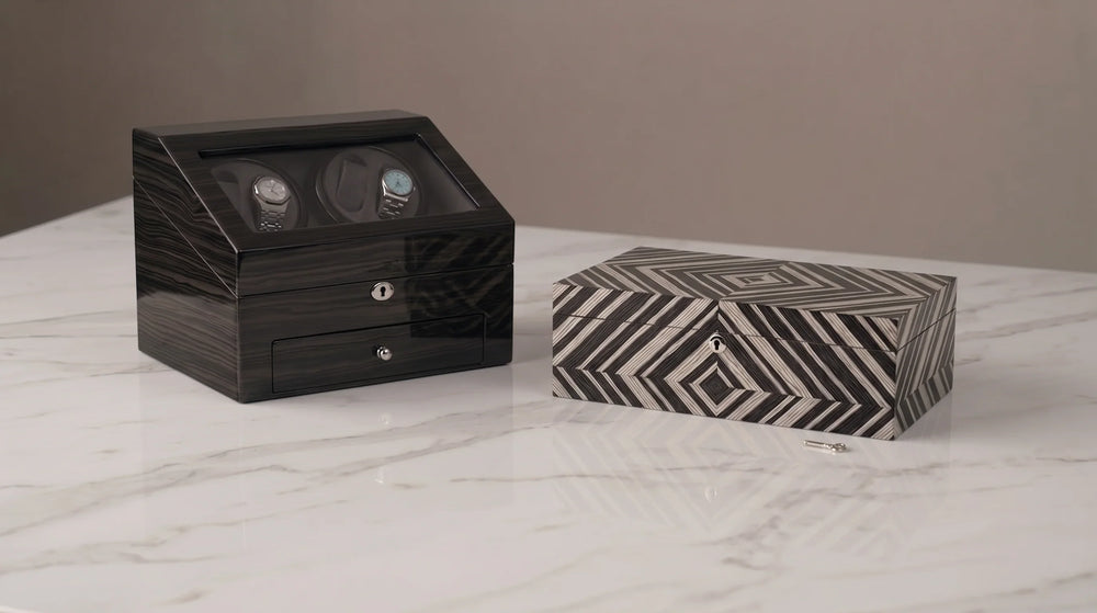 Luxury dark wood watch winder box and geometric patterned jewelry box on a marble surface.