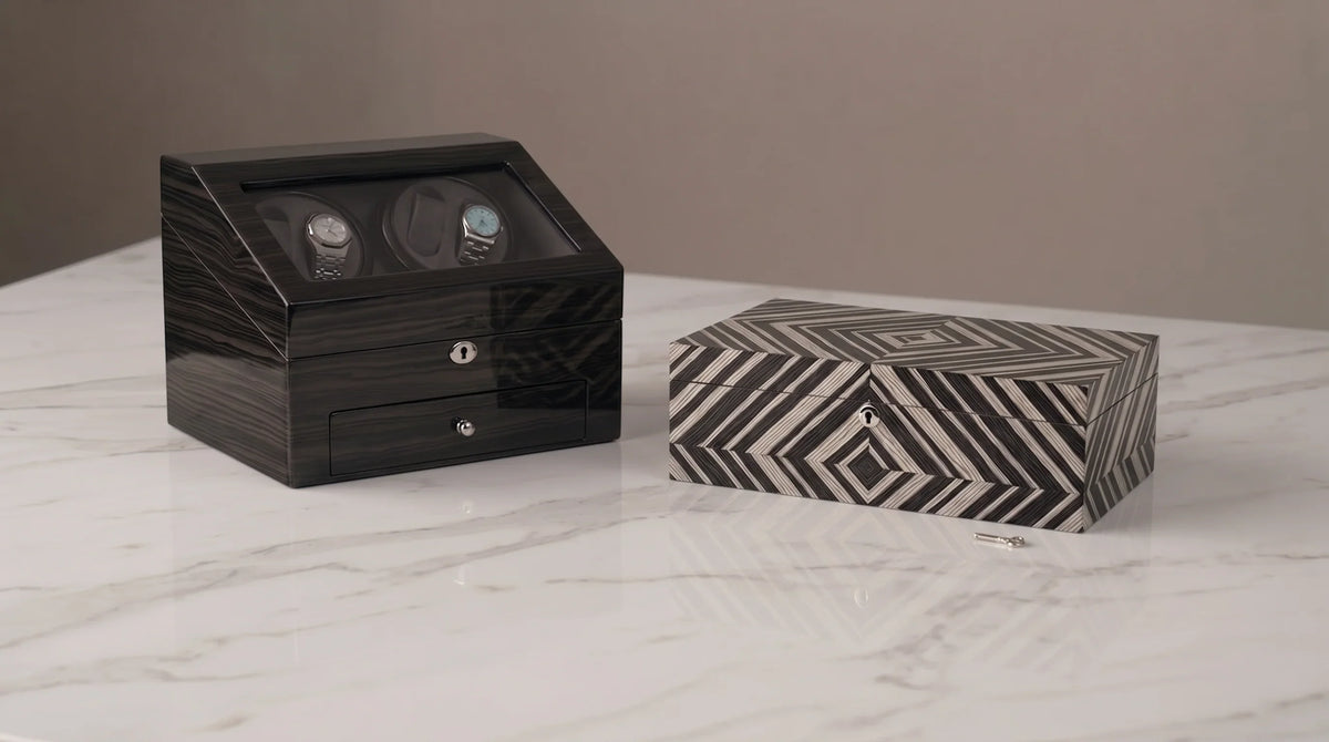 Luxury dark wood watch winder box and geometric patterned jewelry box on a marble surface.