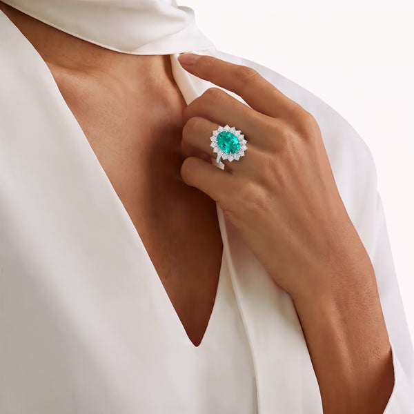Woman wearing a luxury emerald gemstone ring with a diamond halo setting in white gold.