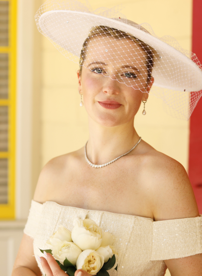 Woman in a white dress and hat with flowers in the background