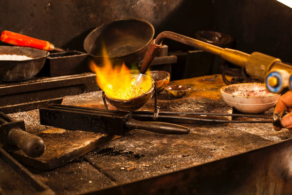 Jeweler using a torch to melt gold in a crucible at a professional jewelry workshop.