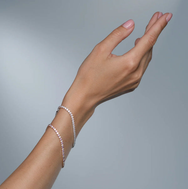 A woman's wrist wearing two luxury diamond tennis bracelets against a grey background.