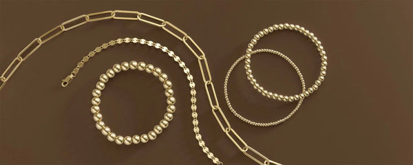 Assorted gold chain necklaces and beaded bracelets arranged on a brown background.