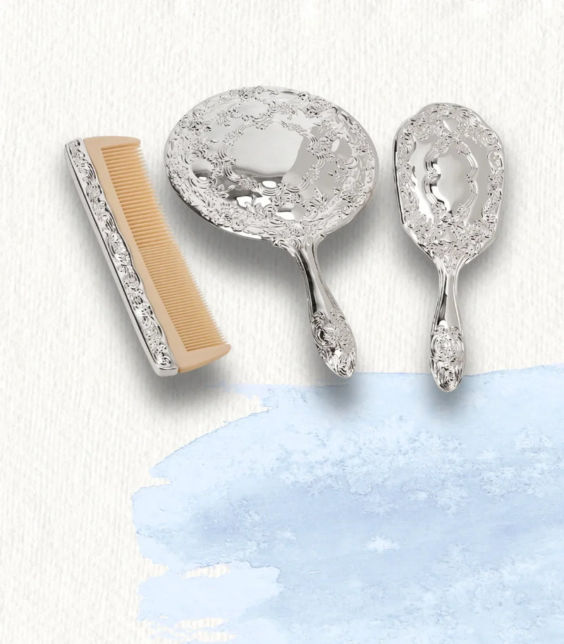 Ornate silver hair comb, handheld mirror, and brush set on a white textured background.