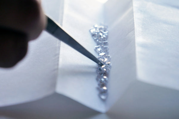 Close-up of tweezers sorting small lab-grown diamonds on a white surface.