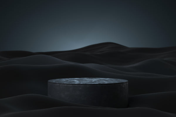 Dark grey stone pedestal on undulating black fabric ripples against a moody background.
