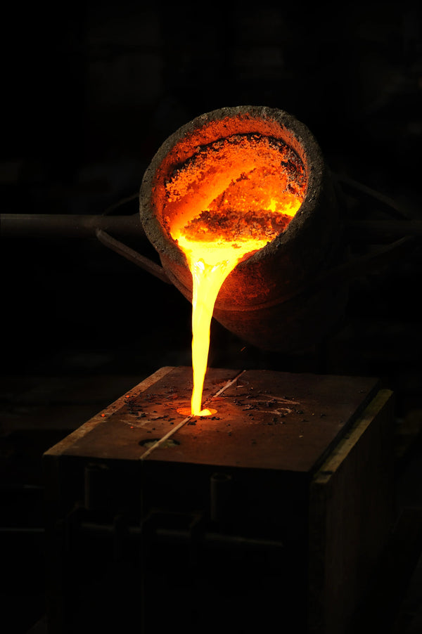 Molten glowing gold being poured from a crucible into a casting mold.