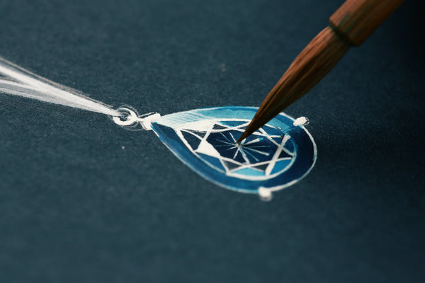 Artist sketching a blue teardrop gemstone pendant design on dark paper.