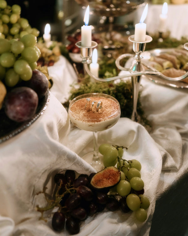 Elegant dessert cocktail in a coupe glass served with fresh grapes and figs on a white cloth.