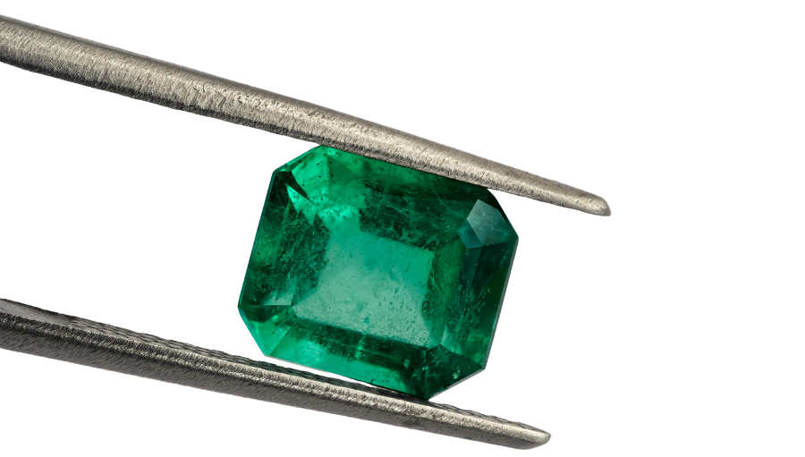 Emerald gemstone held between tweezers on a white background