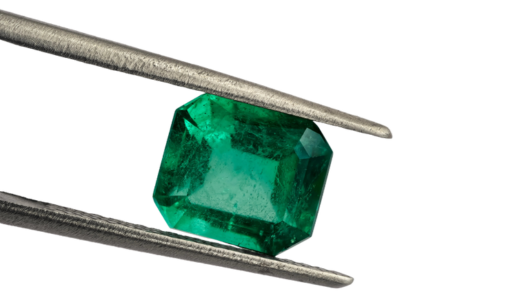 Emerald gemstone held between tweezers on a white background
