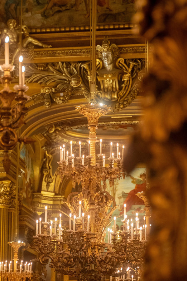 Ornate golden chandeliers with lit candles in a luxurious, classical baroque interior.